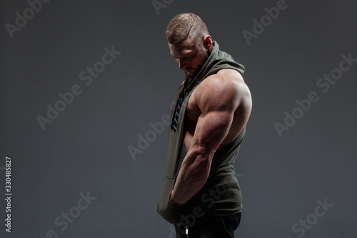 Athletic white man shows muscles side view against a dark background.