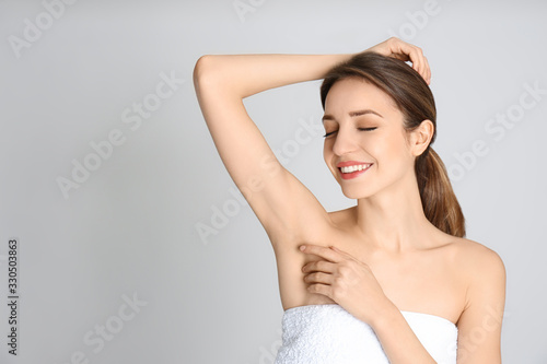 Young woman showing armpit with smooth clean skin on light grey background, space for text