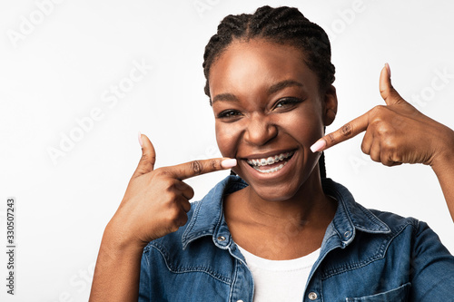 Girl Smiling Pointing Fingers At Brackets On Teeth, Studio Shot