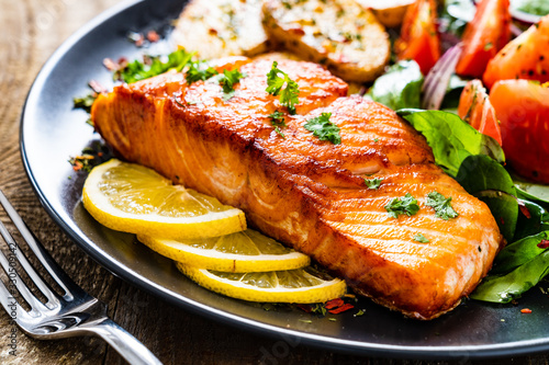 Fried salmon steak with potatoes and vegetables on wooden table