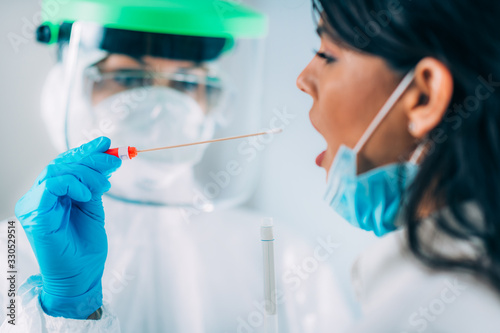 Coronavirus test. Medical worker in protective suite taking a swab for corona virus test, potentially infected young woman