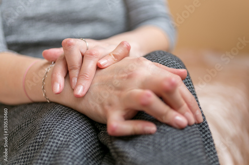 Young woman having rheumatoid arthritis takes a rest sittinng on the couch. Hands and legs are deformed. She feels pain. Selected focus.