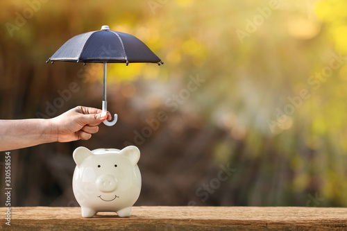 Piggy bank and woman hand hold the black umbrella for protect on sunlight in the public park, to prevent for asset and saving money for buy health insurance concept.