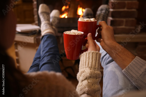 Couple with cups of delicious cocoa resting near fireplace at home, closeup. Winter vacation