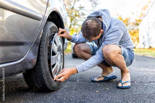 Tire wheel with missing cap cover on parked car with man replacing hubcap with new shiny metal outside