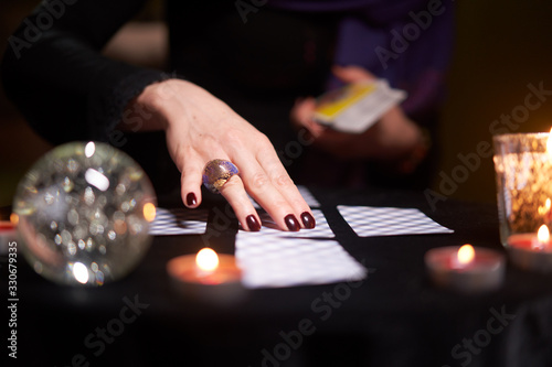 Fortuneteller's hands with cards at table with candles, magic ball in dark room