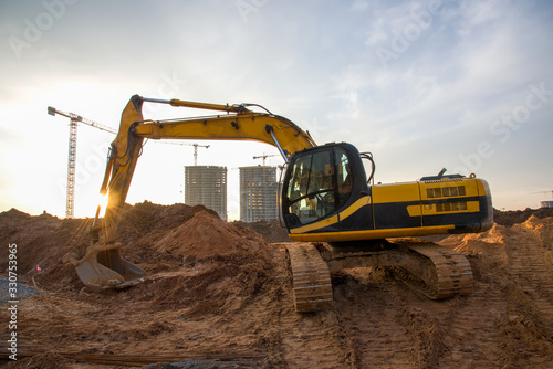 Excavator at earthworks on construction site. Backhoe loader digs a pit for the construction of the foundation. Digging trench for laying sewer pipes drainage in ground. Earth-Moving Heavy Equipment