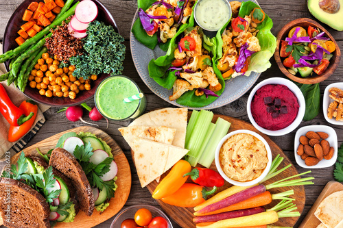 Healthy lunch table scene with nutritious Buddha bowl, lettuce wraps, vegetables, sandwiches and salad. Above view over a wood background.