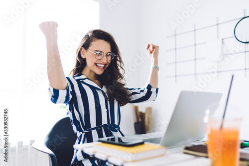 Excited young woman sitting at table with laptop and celebrating success