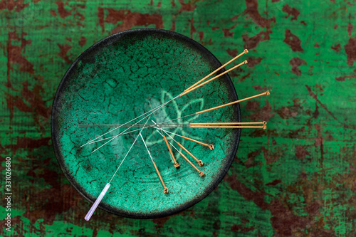 green ceramic Asian Bowl with needles for acupuncture on an old green paint wooden background