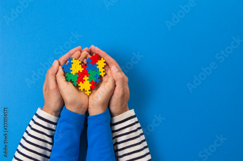 World autism awareness day concept. Adult and child hands holding puzzle heart on light blue background