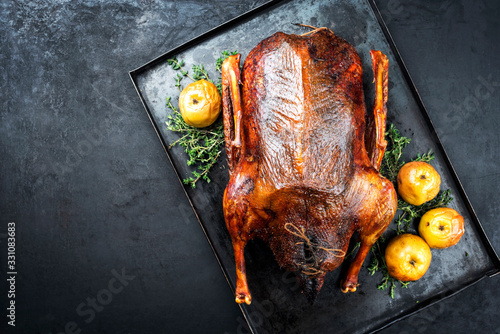 Traditional roasted stuffed Christmas goose with apples and herbs as top view on a rustic metal tray with copy space left