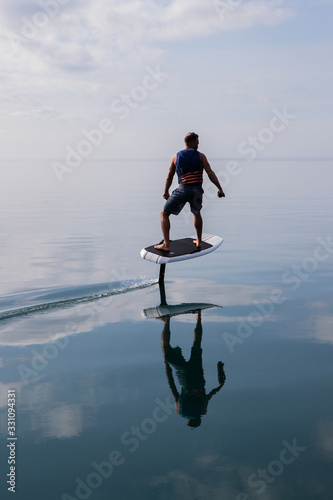 Man riding an electric hydrofoil foil board on a lake with a life jacket