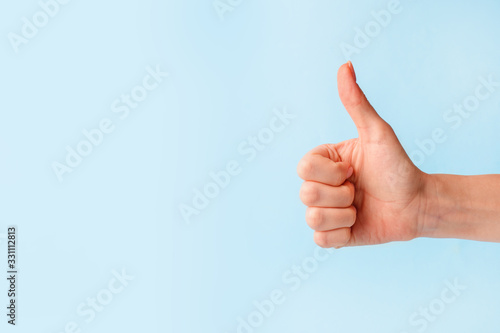 Closeup of female hand showing thumbs up sign against pastel blue background, copy space, minimal concept