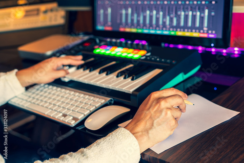 male composer hands writing lyric on paper and creating melody on midi keyboard and computer