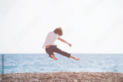 young martial kung fu kid master flying making leg kick in air during sport leisure training activity on sea beach in sunset with copy space