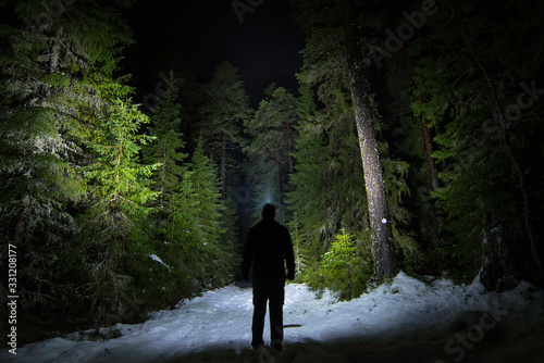 Figure on forest path at night with headlamp illuminating the trees and path