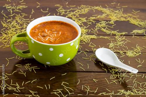 Traditional Turkish vermicelli soup in a green color mug on wooden table with vermicelli grains and spoon.