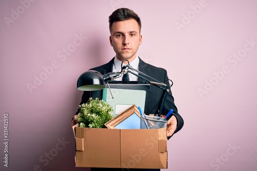 Young handsome caucasian business man holding cardboard box unemployment fired from job with a confident expression on smart face thinking serious