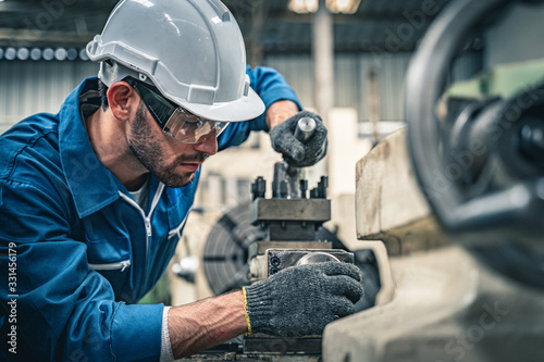 Male engineer in blue jumpsuit and white hard hat operating lathe machine. 