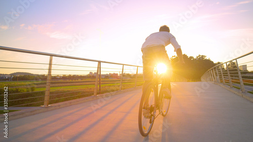 LENS FLARE: Golden morning sun rays shine on man sprinting to work on his bike.