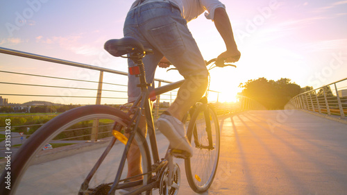 LENS FLARE: Unrecognizable man in a hurry rides his bike across an overpass.