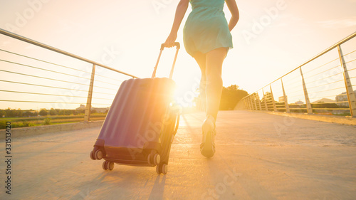 LOW ANGLE: Young tourist with beautiful legs runs to the airport at sunset.