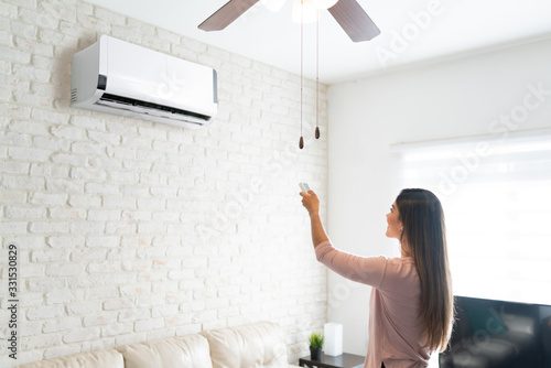 Woman Adjusting Temperature Of Air Conditioner With Remote