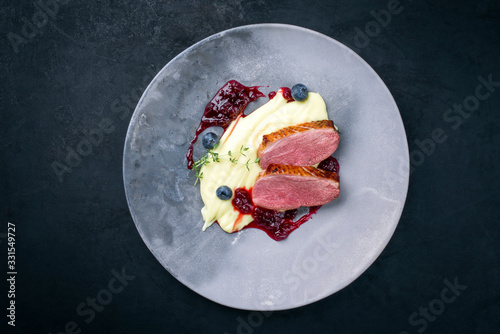 Traditional gourmet duck breast filet with mashed potatoes and cranberry sauce as top view on a modern design plate with copy space