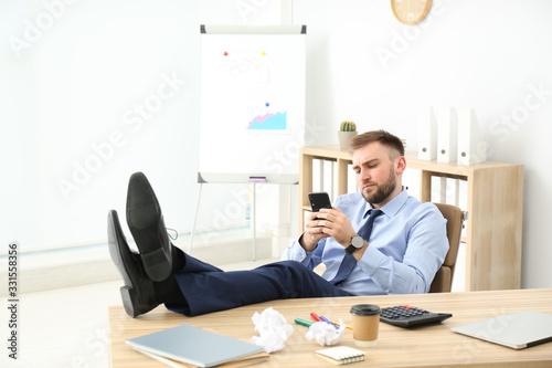 Lazy office employee with mobile phone at workplace