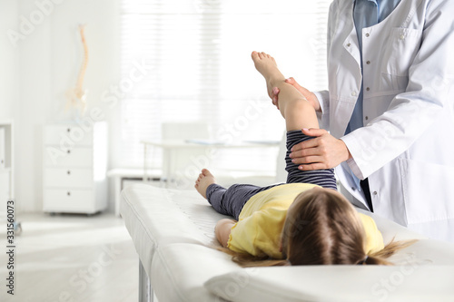 Professional orthopedist examining little patient's leg in clinic