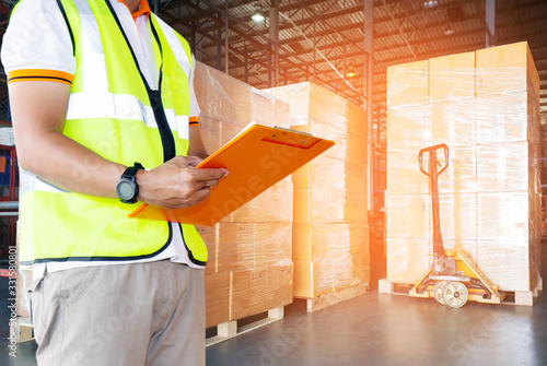 Worker courier holding clipboard writing on paper checklist for delivering shipment pallet goods, package boxes , packaging, cargo export, industry delivery warehouse transport and logistics.
