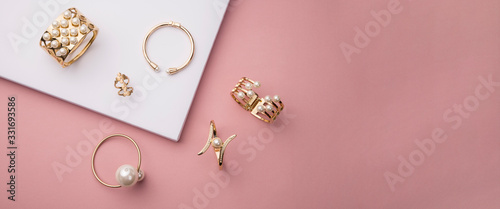 Top view of golden with pearl bracelets on pink and white background with copy space