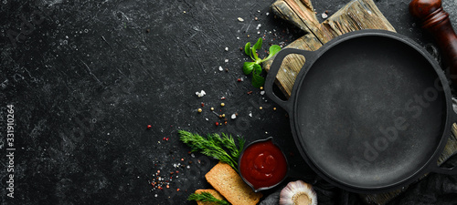 Black frying pan on stone background with vegetables and spices. Top view. Free space for your text. Rustic style.