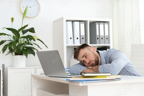 Lazy young man wasting time at table in office