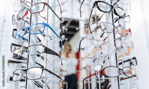 Row of glasses at an opticians. Eyeglasses shop. Stand with glasses in the store of optics. Woman's hand gives glasses to a man. Presenting spectacles