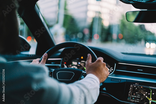 Back cropped view of automobile wheel and male enjoying roadway in contemporary motorized transport for travel, selective focus on autonomous head up during destination driving in comfortable car