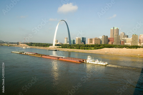 Daytime view of tug boat pushing barge down Mississippi River in front of Gateway Arch and skyline of St. Louis, Missouri as seen from East St. Louis, Illinois on the Mississippi River