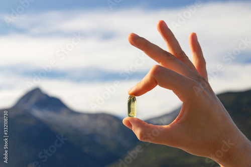 Female hand holds omega 3 capsule. Capsule with fish oil on a background of nature.