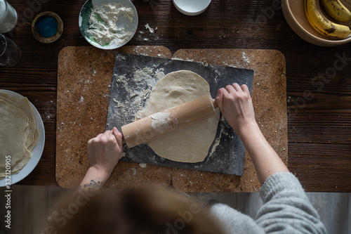 Kobieta robi ciasto. Wałkuje ciasto z mąką na drewnianym stole.