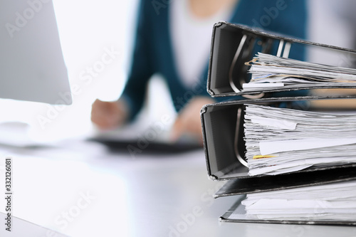 Binders with papers are waiting to be processed by business woman or bookkeeper working at the desk in office back in blur. Audit and tax concept