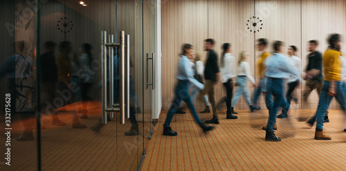 Group of office employees in motion go around at coworking space. People in business center walking at hall. Motion blur. Wide image