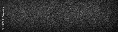 Ultra wide rough black surface. Panoramic background with darkened edges. Texture of flat and grainy sandpaper or panorama of uneven wall material.