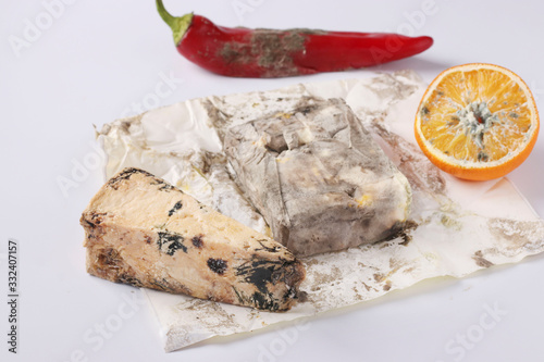 Spoiled rotten foods with mold: orange, pepper, hard cheese and butter on white background