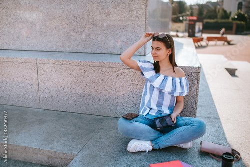A young caucasian beautiful girl sits next to a monument with a tablet in her hand