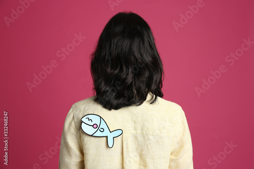 Woman with paper fish on back against pink background. April fool's day