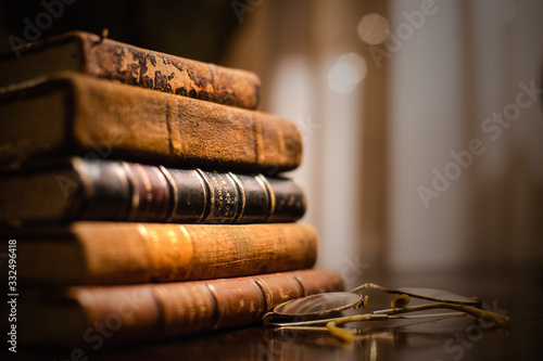 A vintage pile of five old brown leather books with eye glasses on a wood table.