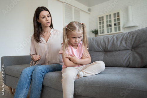 Sad stubborn little girl sit on couch back to mom feel offended avoid talking or listening, angry hurt small preschooler daughter ignore mother speak lecturing or scolding, family fight concept