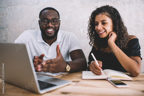 Cheerful african american male and female colleagues discussing project ideas making research on laptop computer, smiling dark skinned man explaining information to female student via webinar