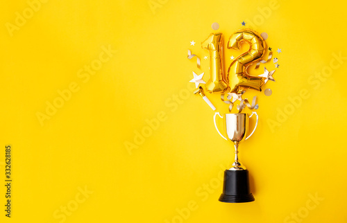 Number 12 gold anniversary celebration balloon exploding from a winning trophy